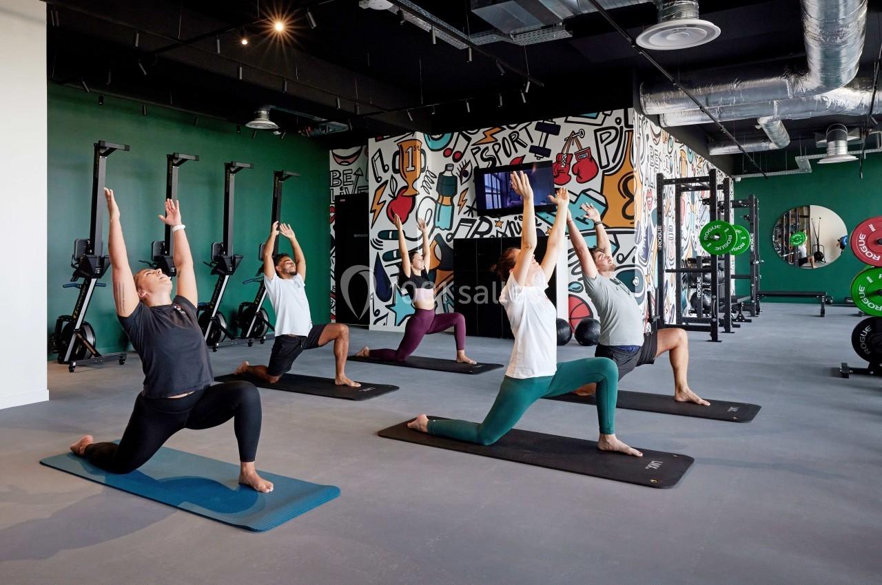 Personnes pratiquant le yoga en groupe dans une salle de sport moderne avec des équipements et un mur décoré de graffitis.