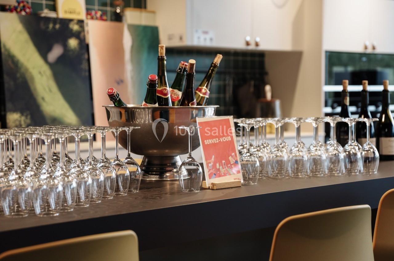 Seau rempli de bouteilles de champagne entouré de verres à pied alignés sur un comptoir dans un espace moderne.