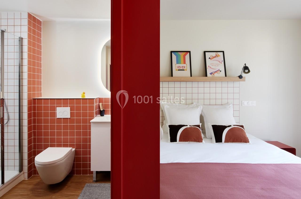 Chambre d'hôtel avec lit double, salle de bain attenante à carreaux rouges et décoration murale colorée.