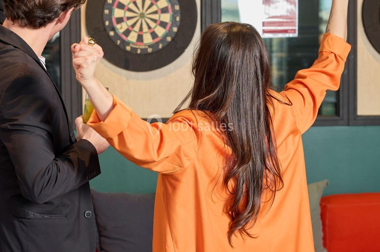 Deux personnes de dos célèbrent devant une cible de fléchettes dans un espace intérieur avec canapé et table basse.