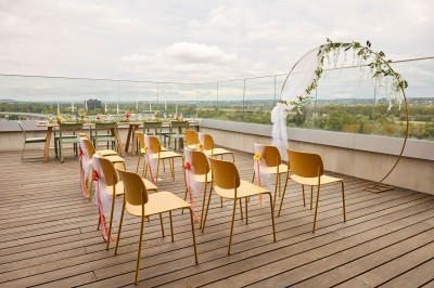 Un couple célèbre son mariage sur une petite scène décorée de voiles et de feuillages, devant une fresque colorée.