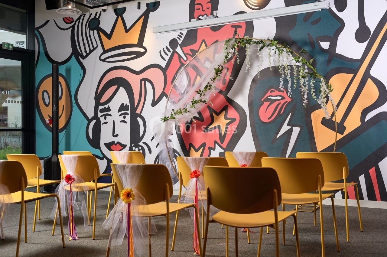 Chaises jaunes alignées dans une salle décorée de fresques colorées et d'une arche ornée de fleurs.