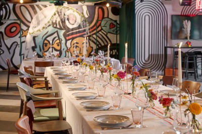 Un couple célèbre son mariage sur une petite scène décorée de voiles et de feuillages, devant une fresque colorée.