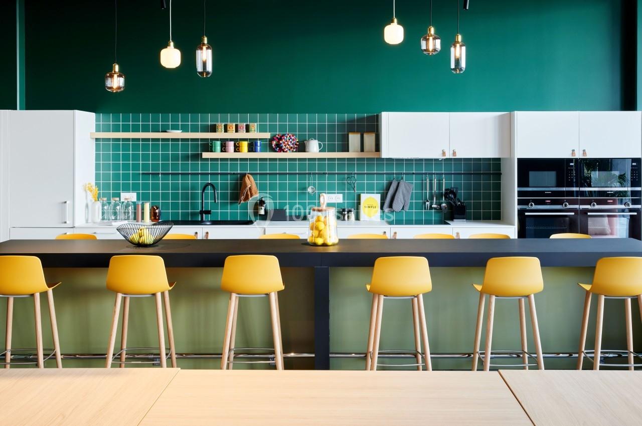 Cuisine moderne avec un mur vert, des armoires blanches, un îlot noir et des tabourets jaunes alignés.