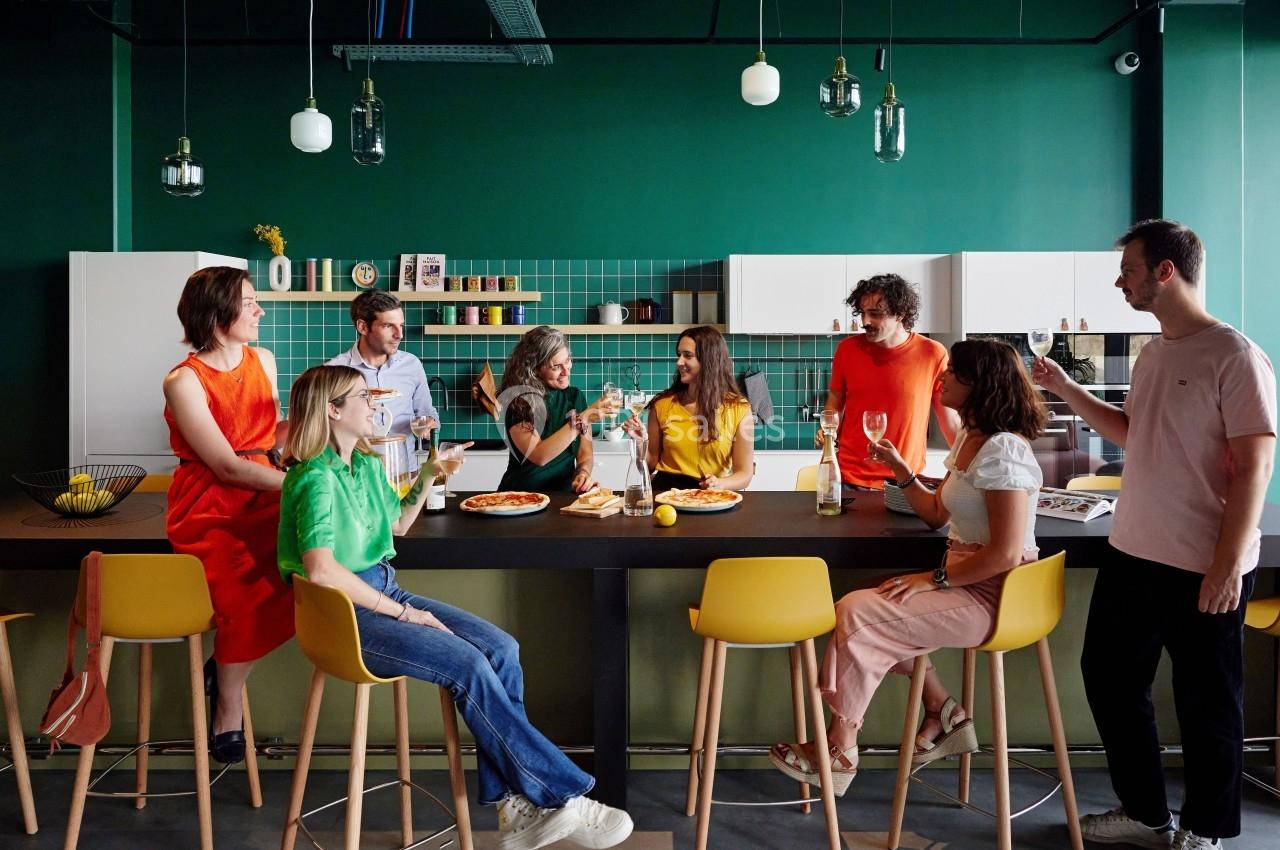 Un groupe de personnes assises et debout autour d'un comptoir dans une cuisine moderne, partageant un repas.