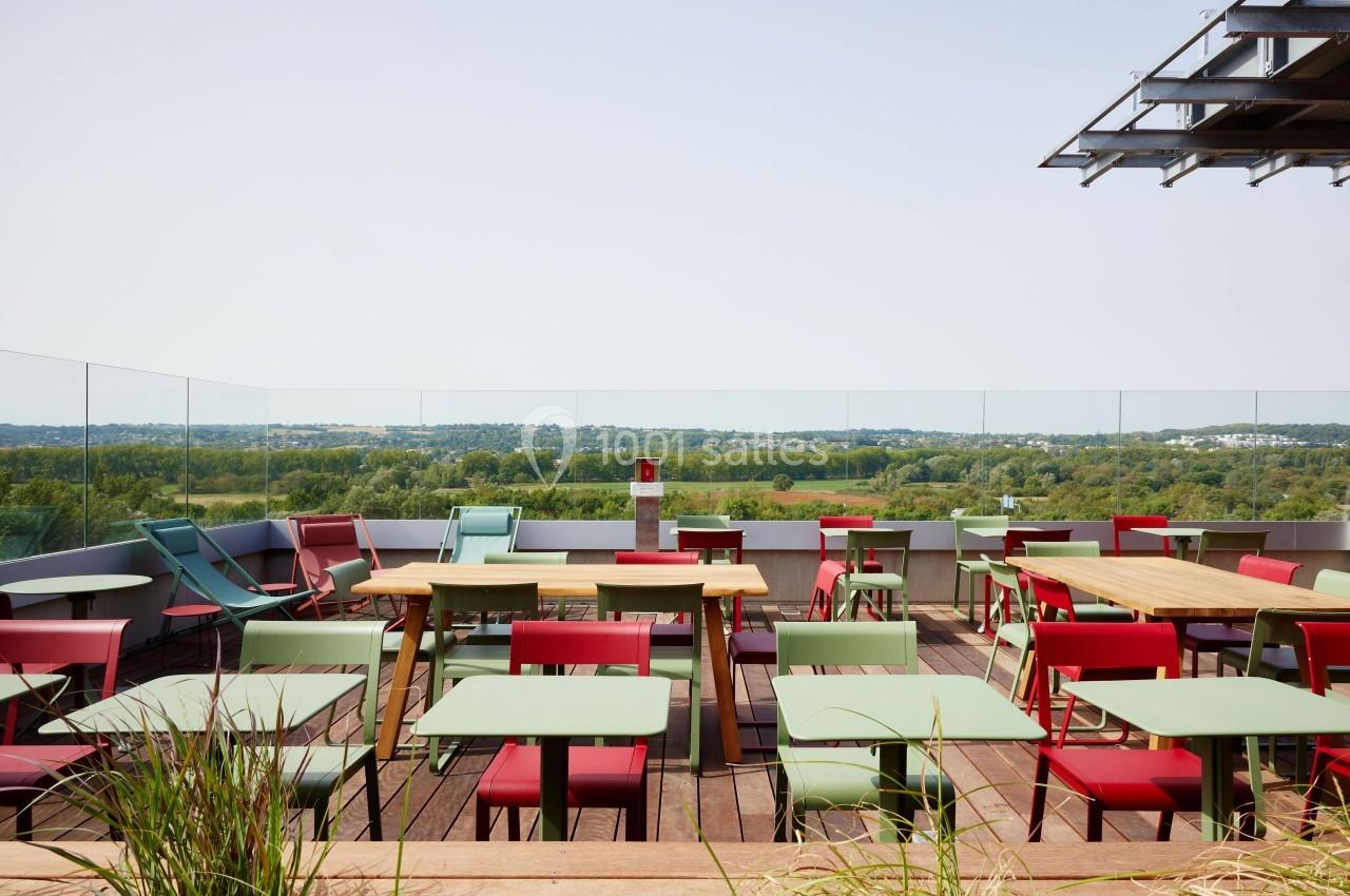 Terrasse avec des tables et chaises colorées, vue dégagée sur un paysage verdoyant sous un ciel clair.