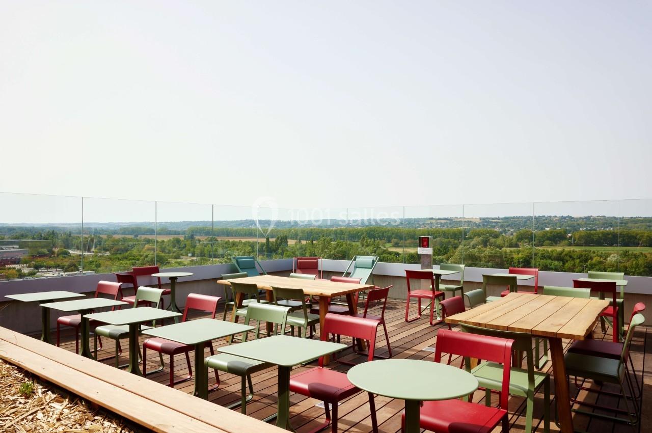 Terrasse avec tables et chaises colorées, vue dégagée sur un paysage verdoyant sous un ciel clair.