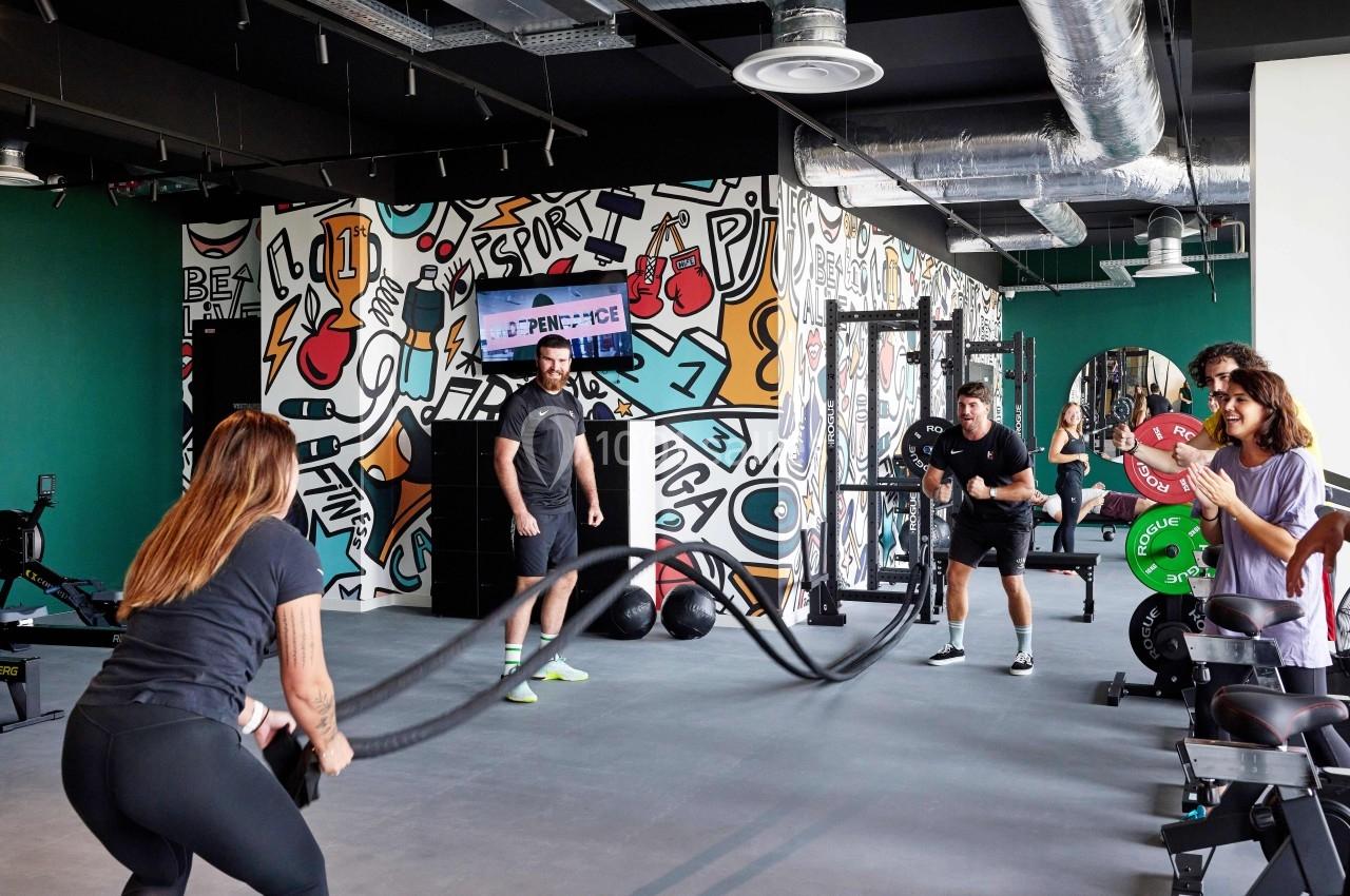 Des personnes s'entraînent dans une salle de sport moderne avec des cordes ondulatoires, sous le regard d'un coach.