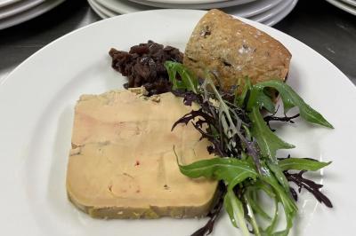 Homme en veste de chef blanche, debout devant une architecture en pierre et des grilles métalliques.