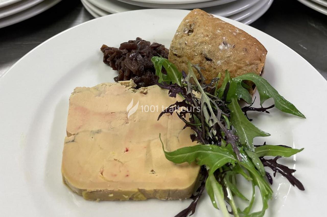 Assiette avec tranche de foie gras, confit d'oignons, pain aux céréales et salade verte sur un fond de table dressée.