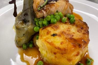 Homme en veste de chef blanche, debout devant une architecture en pierre et des grilles métalliques.