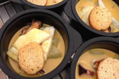 Homme en veste de chef blanche, debout devant une architecture en pierre et des grilles métalliques.