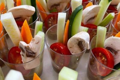 Homme en veste de chef blanche, debout devant une architecture en pierre et des grilles métalliques.