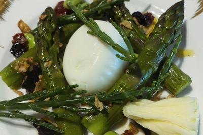 Homme en veste de chef blanche, debout devant une architecture en pierre et des grilles métalliques.
