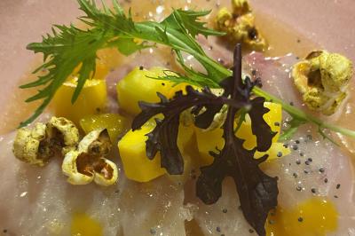 Homme en veste de chef blanche, debout devant une architecture en pierre et des grilles métalliques.