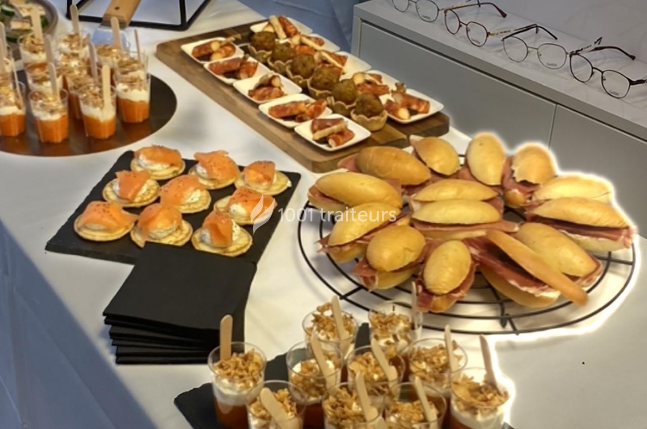 Buffet avec verrines, canapés au saumon, mini-sandwiches et amuse-bouches variés sur une table blanche.