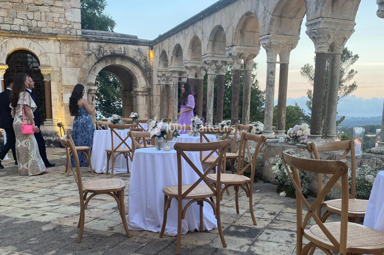 Tables décorées pour un événement en plein air, entourées d'arcades en pierre et de végétation, au crépuscule.