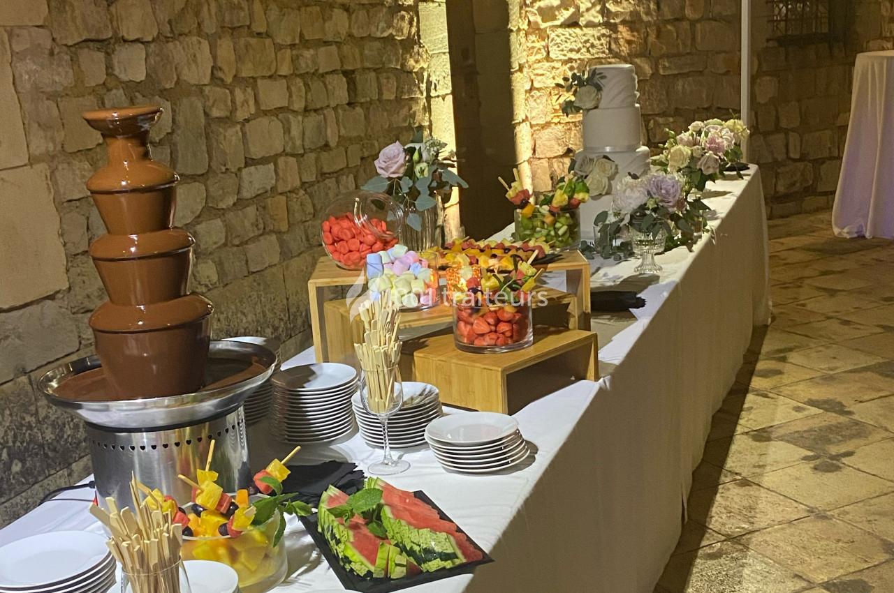 Buffet avec fontaine de chocolat, brochettes de fruits, gâteaux décorés et assiettes sur une table dans un cadre en pierre.
