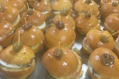 Homme en veste de chef blanche, debout devant une architecture en pierre et des grilles métalliques.