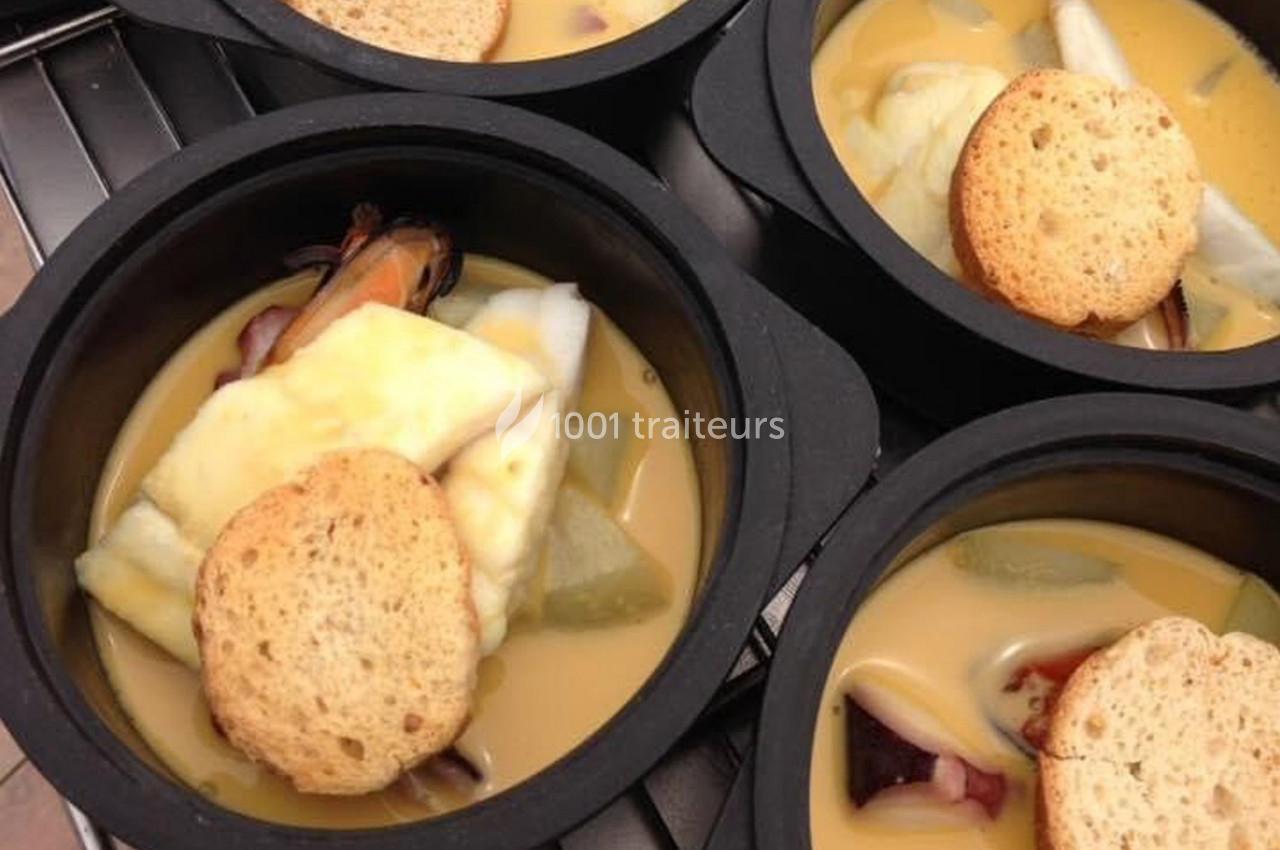 Des bols de soupe de poisson garnis de croûtons et de morceaux de fruits de mer, servis dans des récipients noirs.