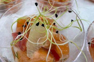 Homme en veste de chef blanche, debout devant une architecture en pierre et des grilles métalliques.