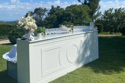 Homme en veste de chef blanche, debout devant une architecture en pierre et des grilles métalliques.
