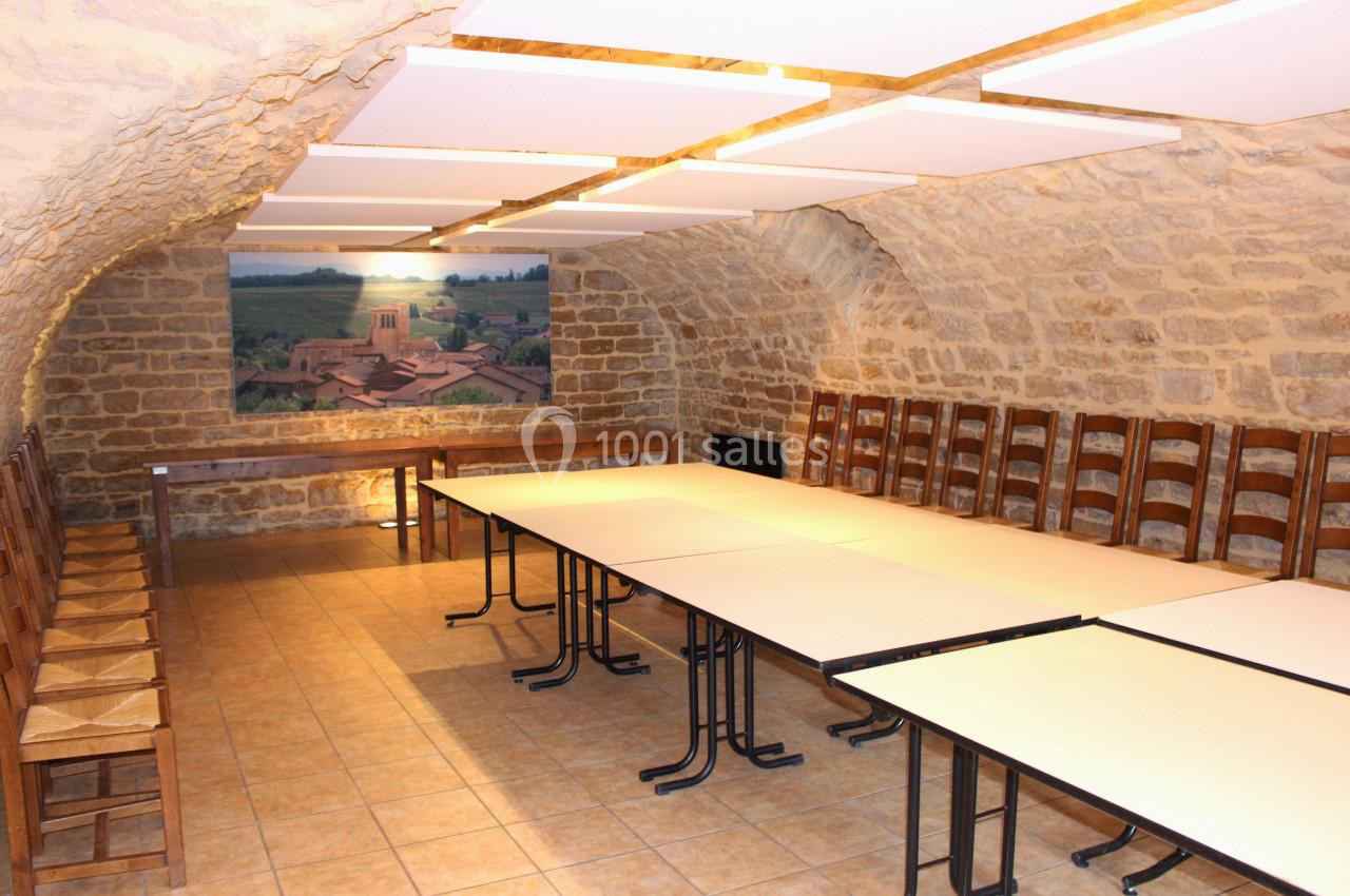 Salle voûtée en pierre avec tables rectangulaires alignées et chaises en bois, décorée d'une grande photo murale.