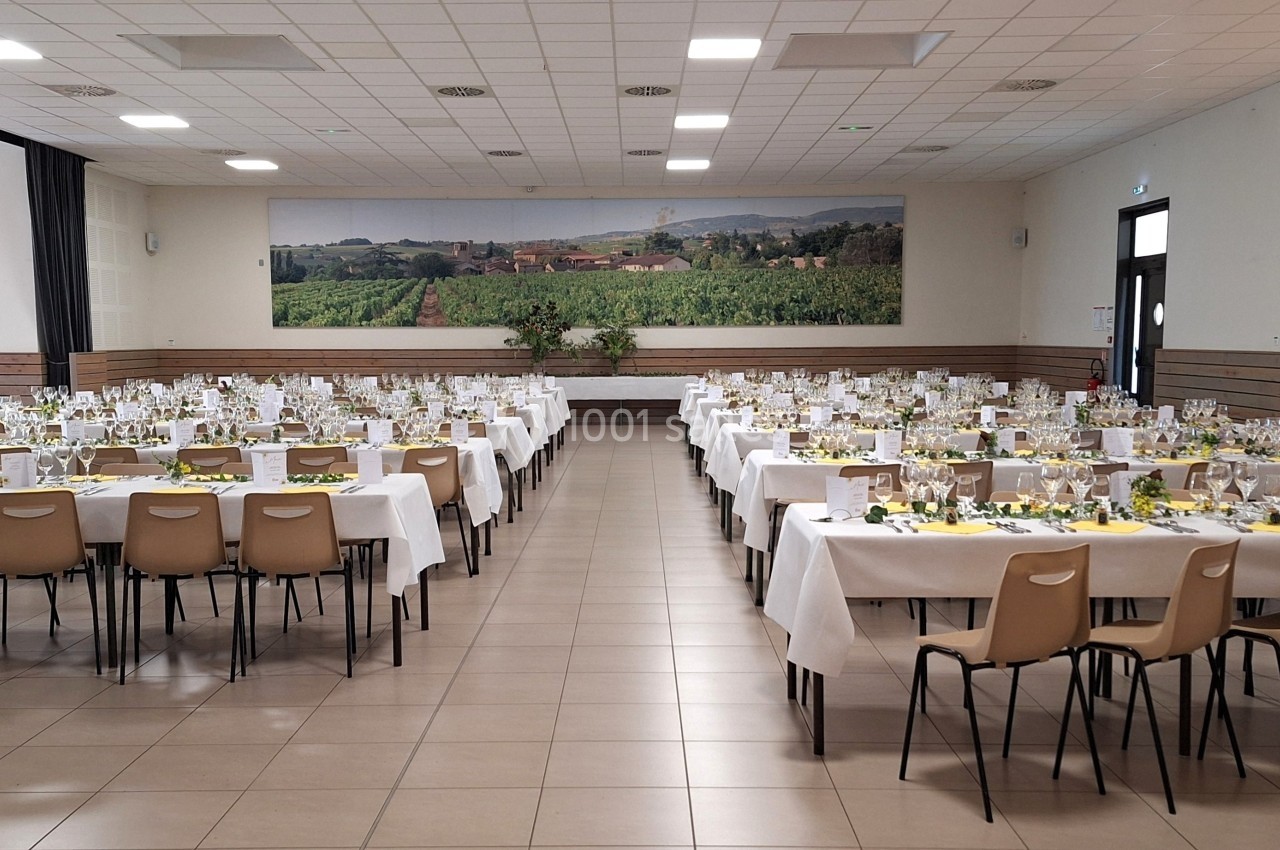 Salle de réception aménagée avec des tables dressées pour un grand événement, décorées de nappes blanches et de touches…