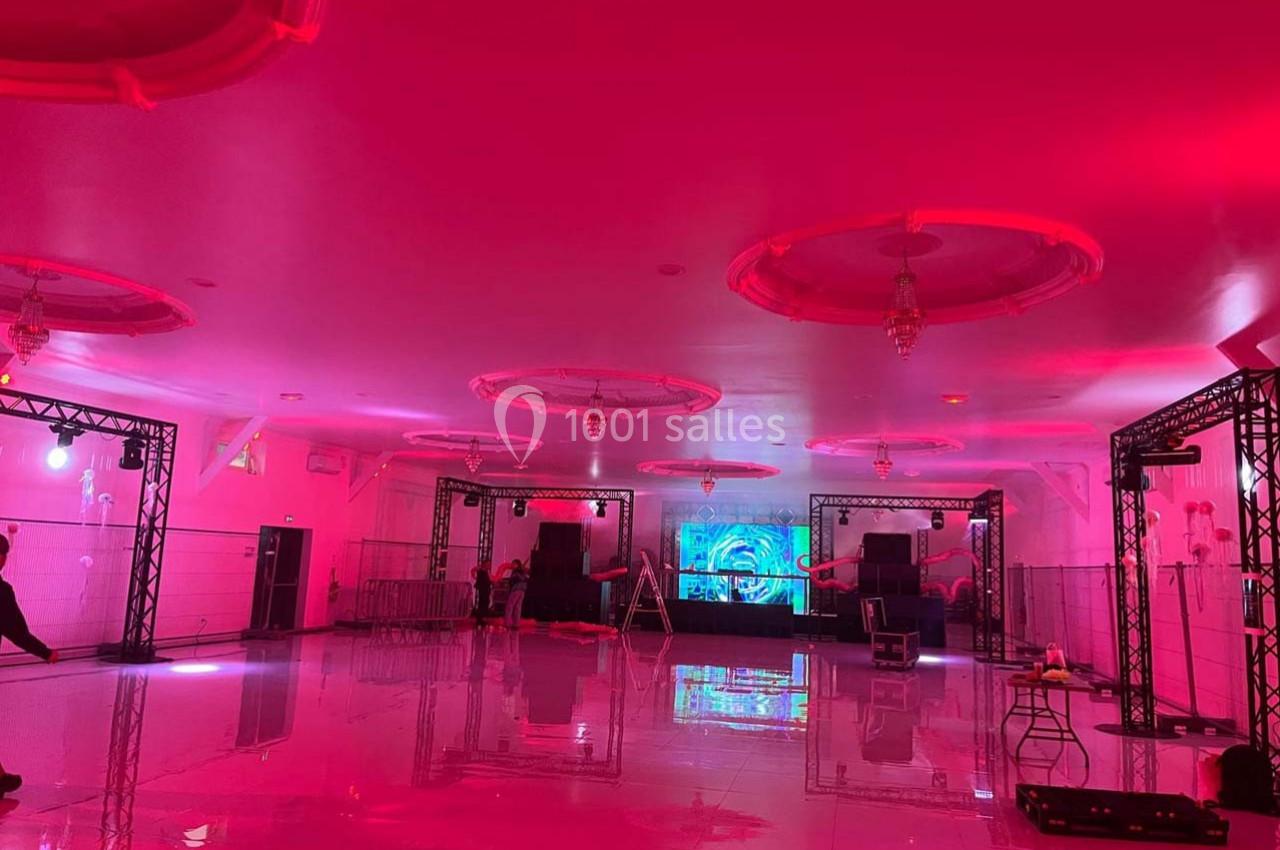 Salle de réception vide éclairée par des lumières roses, avec une scène équipée de matériel audio et visuel.