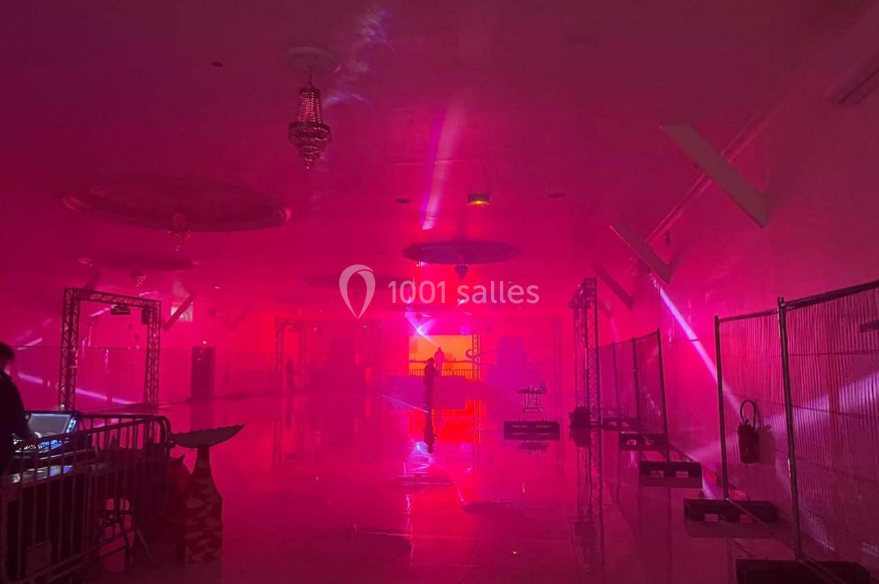 Salle plongée dans une lumière rouge avec des projecteurs, des structures métalliques et un sol réfléchissant.