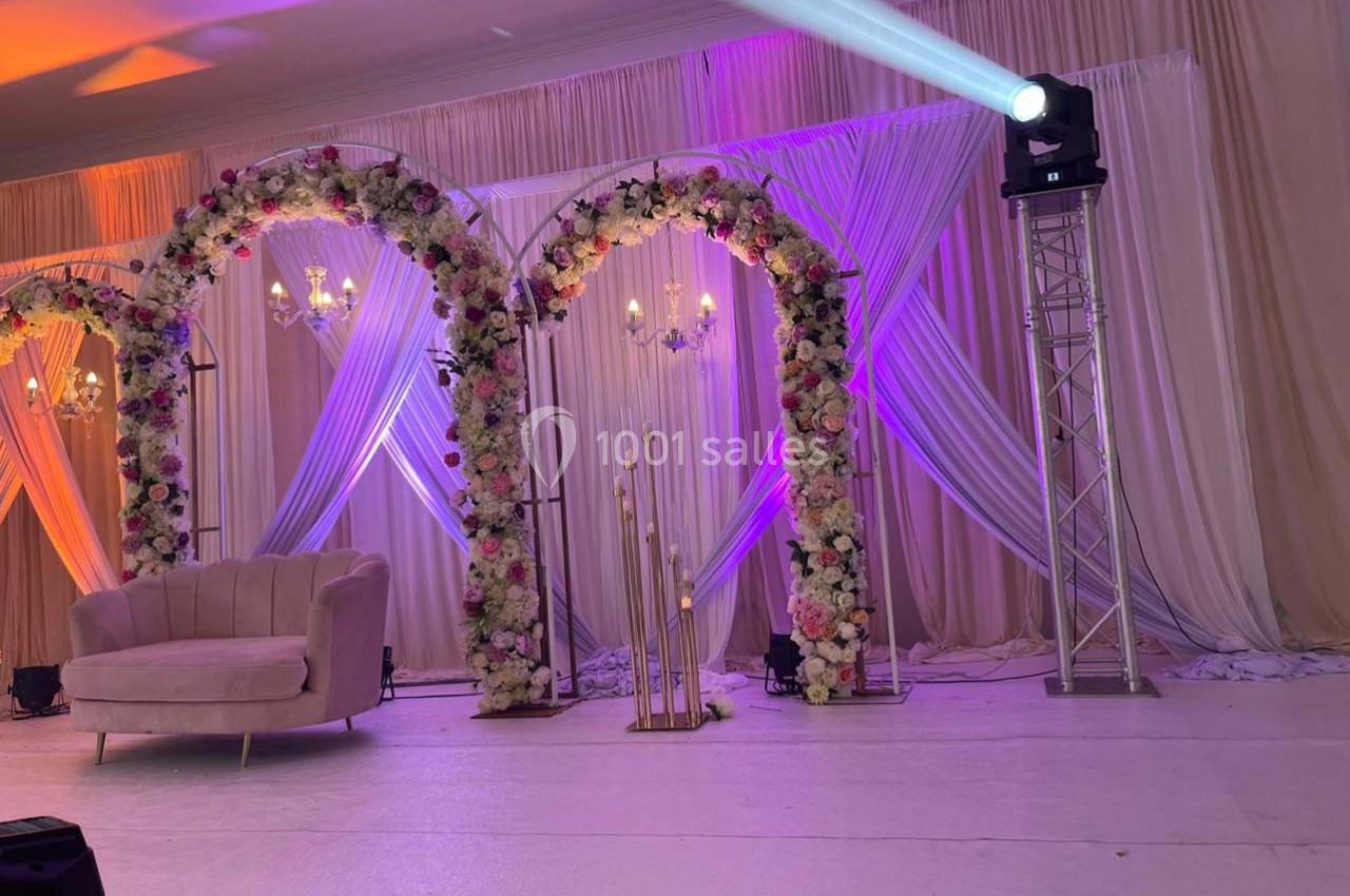 Arches décorées de fleurs, rideaux drapés et éclairage coloré dans une salle de réception élégante.
