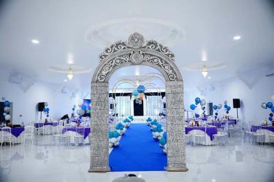 Bâtiment moderne avec façade noire, terrasse aménagée, murs végétalisés et sculptures, sous un ciel nuageux.