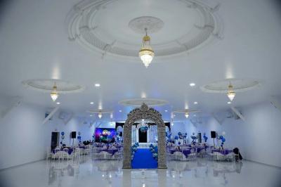 Bâtiment moderne avec façade noire, terrasse aménagée, murs végétalisés et sculptures, sous un ciel nuageux.