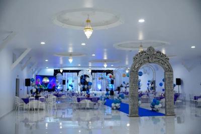 Bâtiment moderne avec façade noire, terrasse aménagée, murs végétalisés et sculptures, sous un ciel nuageux.