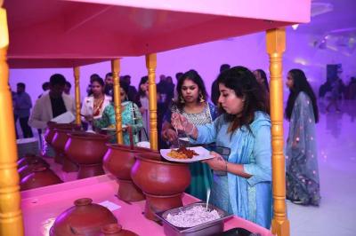 Bâtiment moderne avec façade noire, terrasse aménagée, murs végétalisés et sculptures, sous un ciel nuageux.