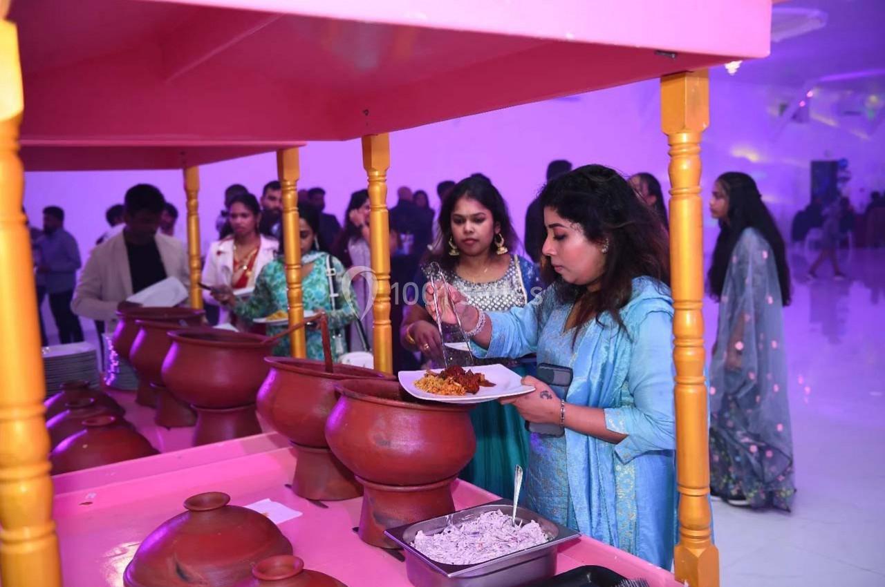 Des personnes se servent de plats dans un buffet avec des pots en terre cuite, dans une salle éclairée en violet.