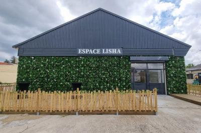 Bâtiment moderne avec façade noire, terrasse aménagée, murs végétalisés et sculptures, sous un ciel nuageux.
