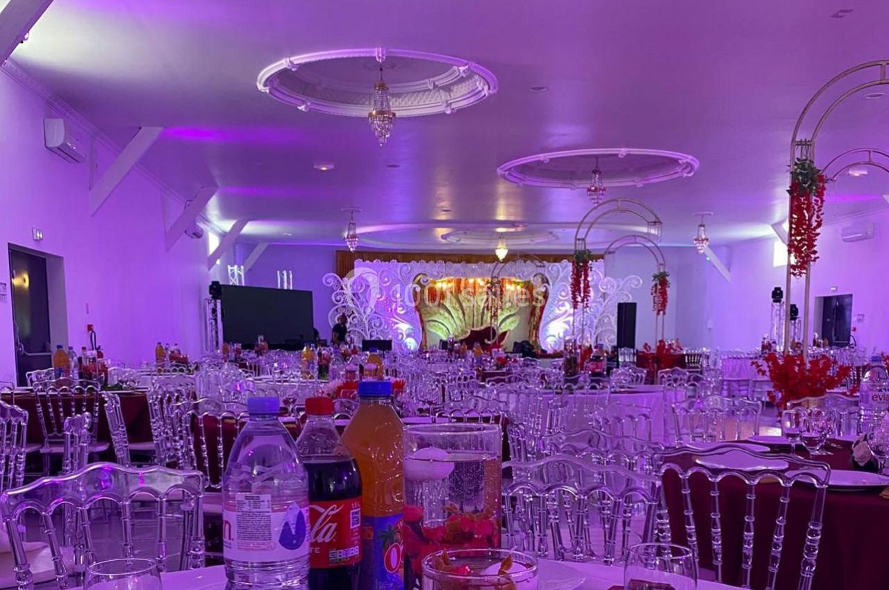 Salle de réception décorée avec des tables dressées, éclairage violet et une scène ornée en arrière-plan.