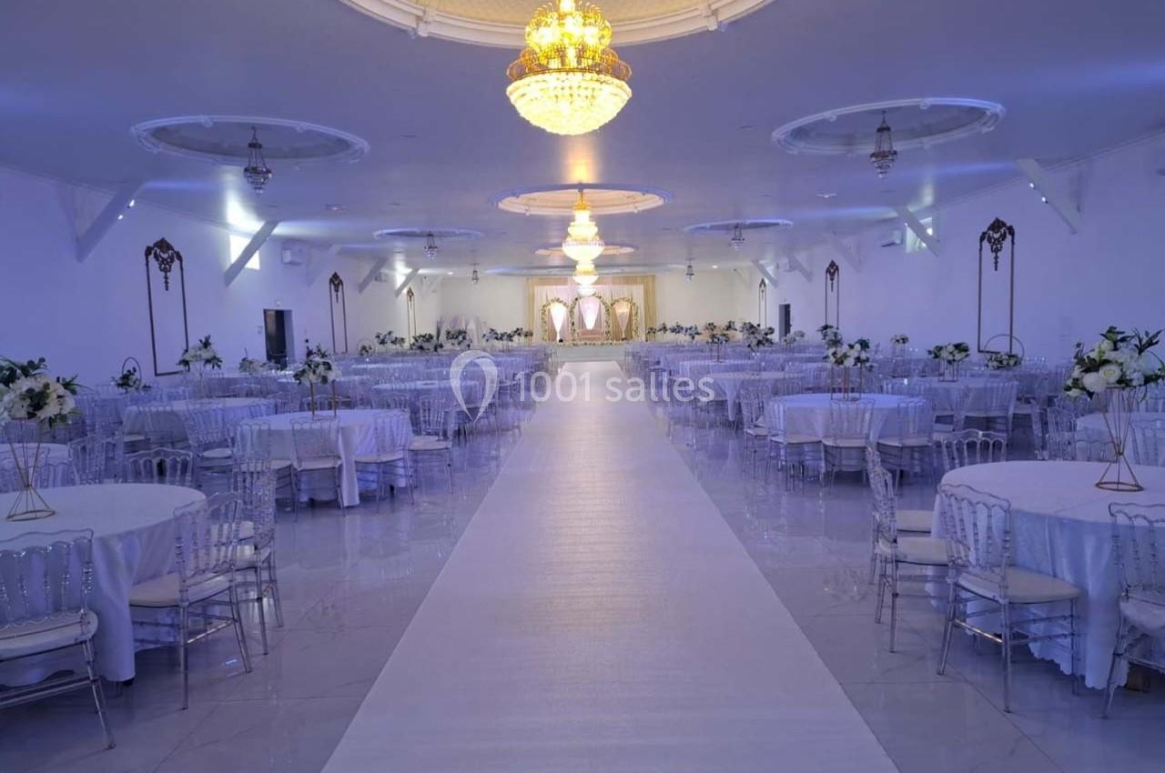 Salle de réception élégante avec tables décorées de fleurs blanches, allée centrale et lustres suspendus.