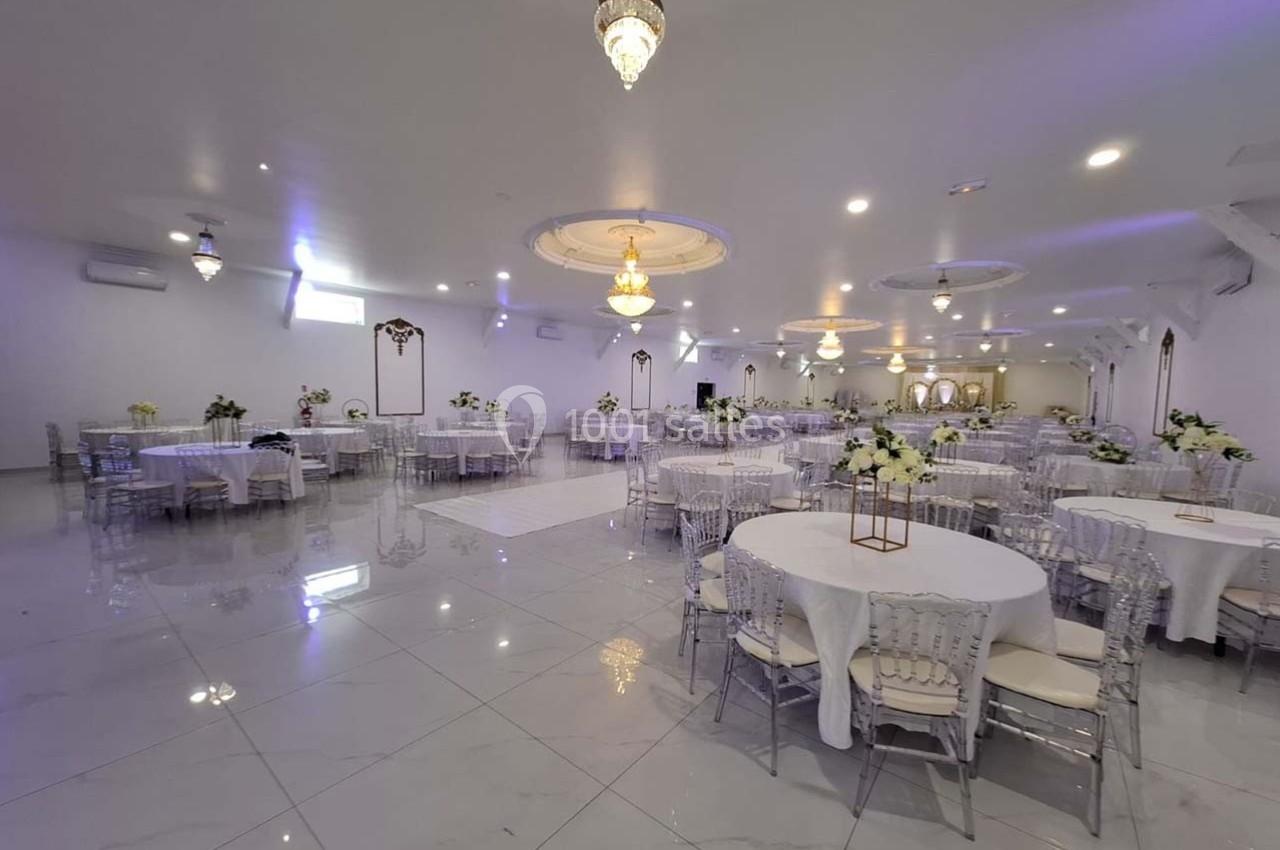 Salle de réception spacieuse avec tables rondes décorées de fleurs blanches et éclairage élégant.