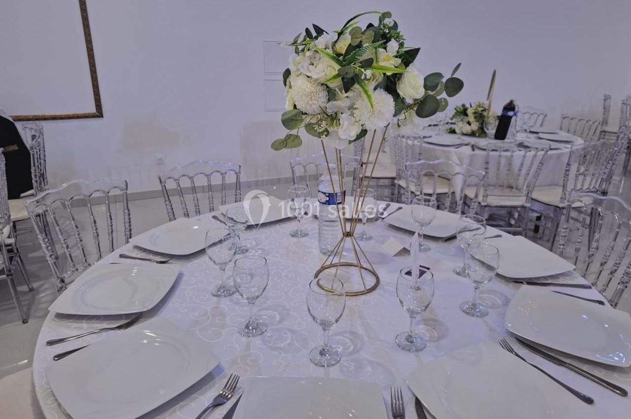 Table ronde dressée avec une nappe blanche, vaisselle élégante et un centre de table floral blanc et vert.