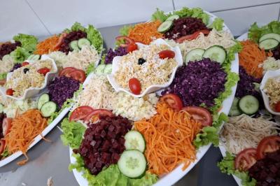 Bâtiment moderne avec façade noire, terrasse aménagée, murs végétalisés et sculptures, sous un ciel nuageux.