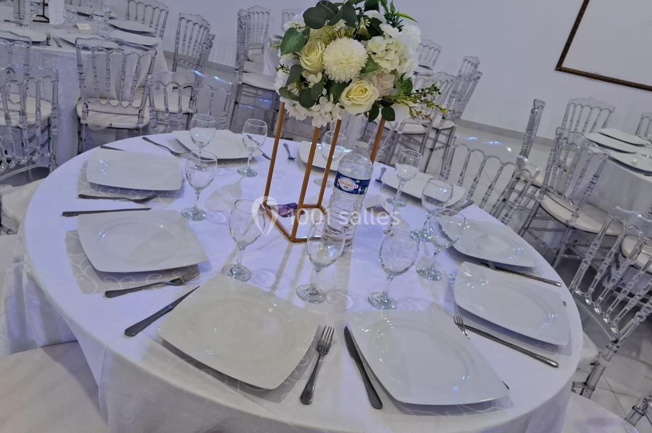 Table ronde dressée avec une nappe blanche, vaisselle blanche, verres, couverts et centre de table floral.