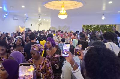 Bâtiment moderne avec façade noire, terrasse aménagée, murs végétalisés et sculptures, sous un ciel nuageux.
