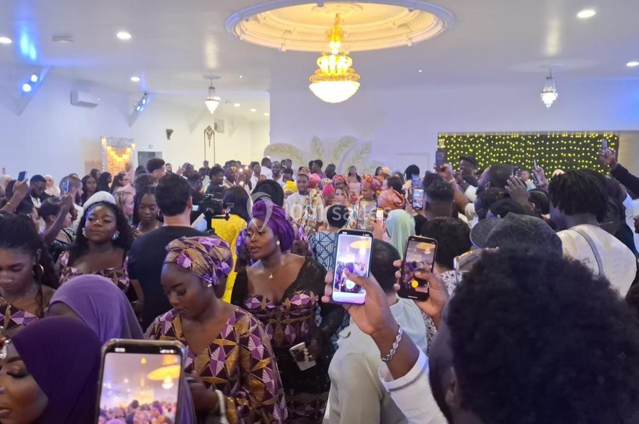 Groupe de personnes en tenue traditionnelle dans une salle éclairée, certaines prenant des photos avec leurs téléphones.
