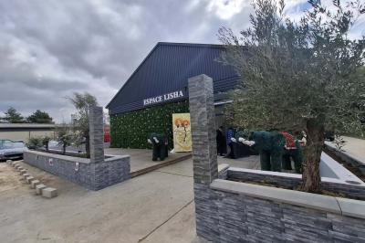 Bâtiment moderne avec façade noire, terrasse aménagée, murs végétalisés et sculptures, sous un ciel nuageux.