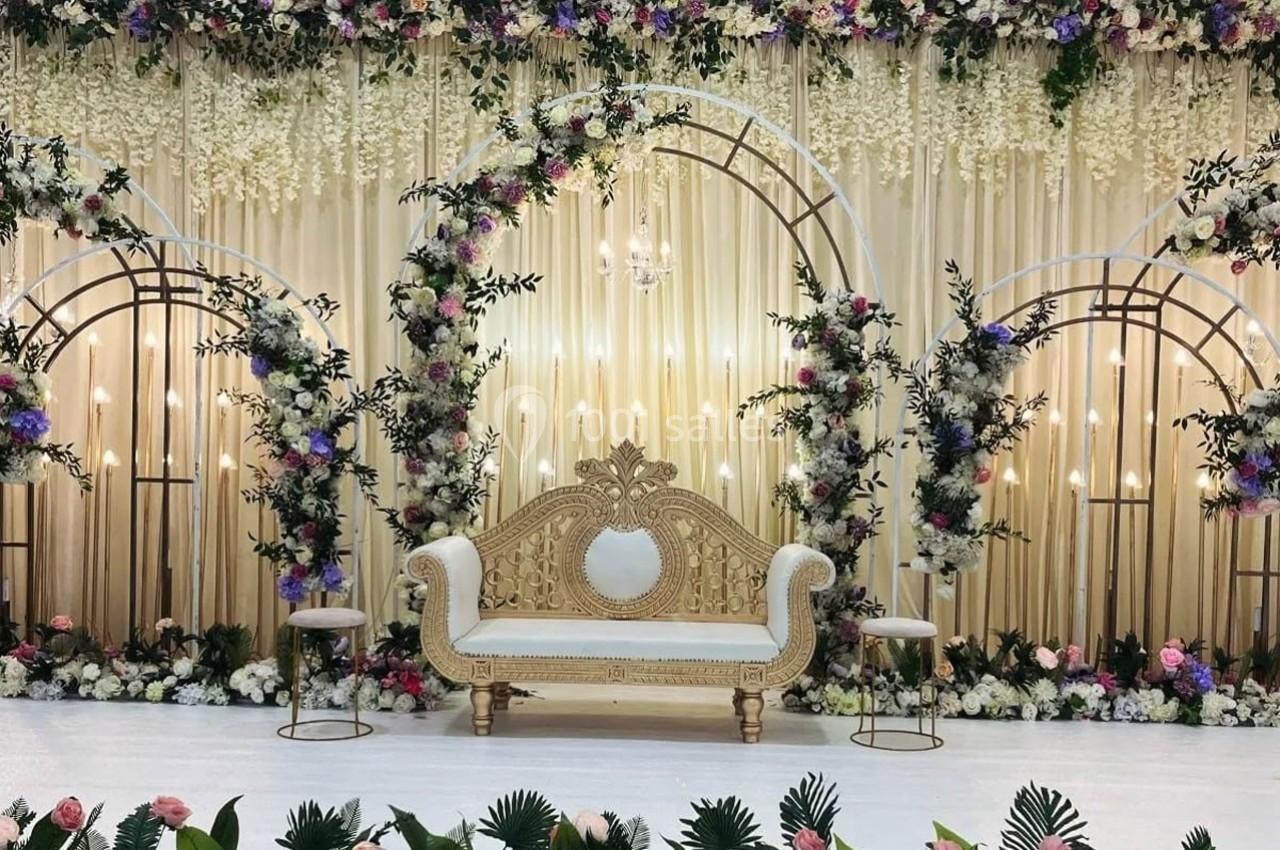 Décor de cérémonie avec un canapé doré, arches fleuries, rideaux beige et compositions florales colorées.
