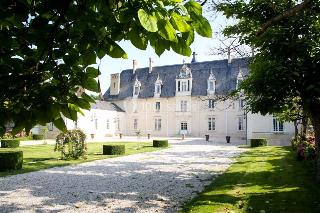 Façade d'un manoir historique entouré d'un jardin verdoyant avec allée gravillonnée et arbustes taillés.