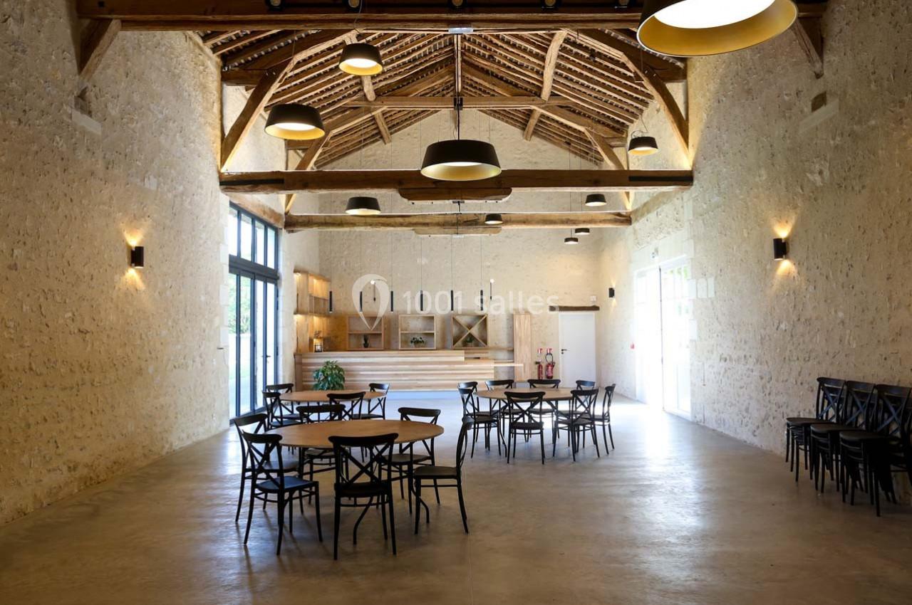 Salle spacieuse avec murs en pierre, poutres apparentes, tables et chaises en bois, éclairage suspendu moderne.