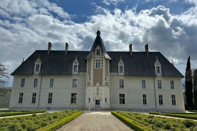Façade d'un château avec une tour centrale et des fenêtres, entouré de végétation.